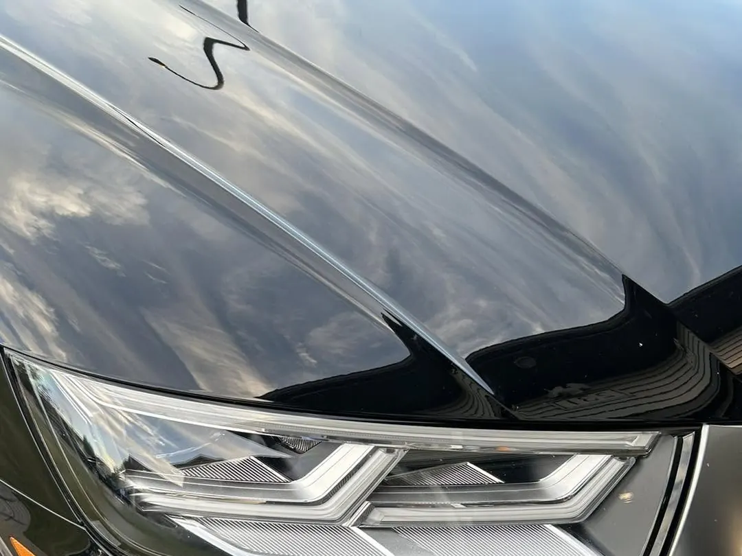 Sky reflections on the glossy black hood of a detailed vehicle